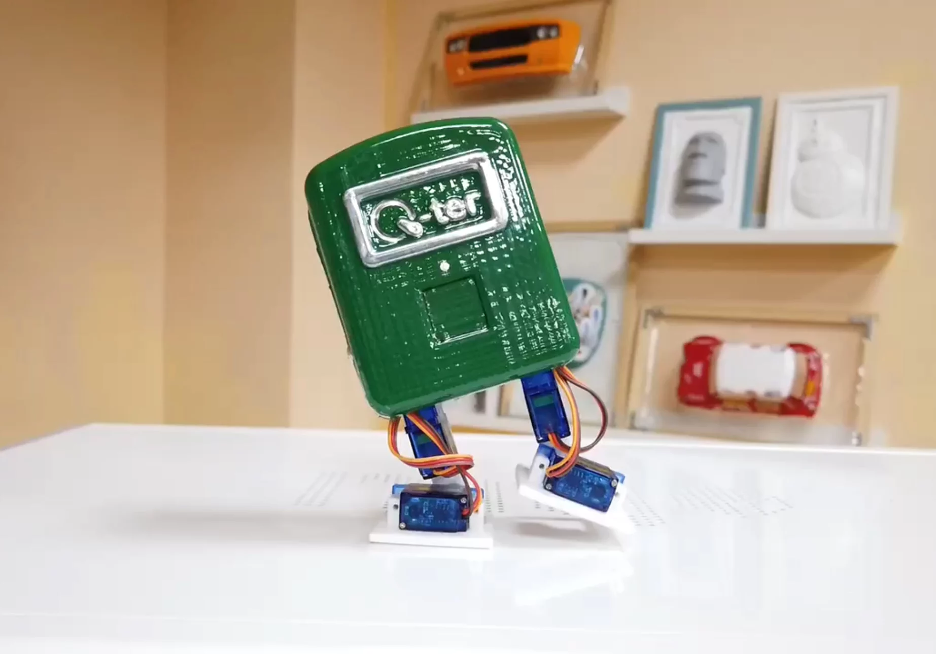 A small robot wearing a green plastic enclosure dancing on a white surface.