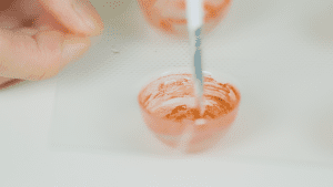 A hand using a brush to apply red color onto the inside of a chocolate mold, preparing for chocolate molding