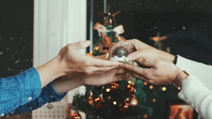 2つの手がクリスマスギフトを交換している。背景には美しく飾られたクリスマスツリーがあり、温かく愛に満ちた雰囲気を演出している