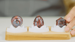 Three molded chocolates placed on a white chocolate display stand, with red and black marbled patterns on the surface, giving a unique artistic look