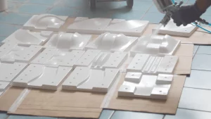 A worker is spray painting the off-road track molds, with completed white vacuum-formed molds placed around, ready for further processing.