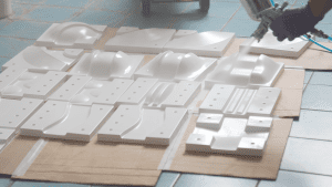 A worker is spray painting the off-road track molds, with completed white vacuum-formed molds placed around, ready for further processing.