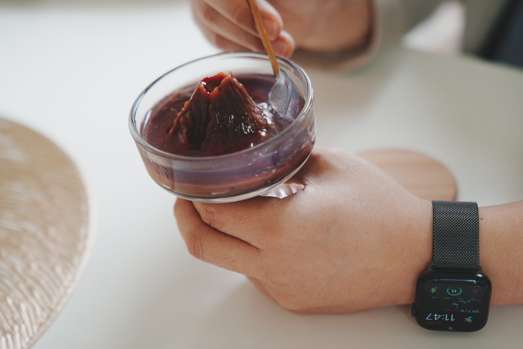 Holding a glass bowl with 'volcano-shaped yokan,' enjoying the dessert with a spoon.