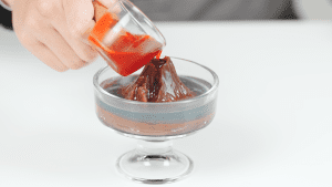 Pouring red fruit sauce into the volcano-shaped yokan mold, finishing the decoration of the dessert.