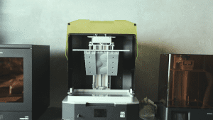 Phrozen Sonic Mega 8K 3D printer is printing an off-road car mold, showing the high-resolution printing process. Another 3D printer is seen beside it.