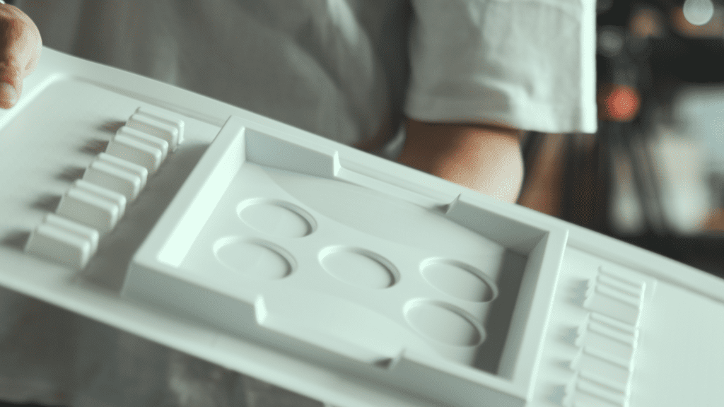 A worker is holding a vacuum-formed off-road track mold, showcasing the details of the mold, including multiple circular indentations and linear structures.