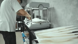 Mass production of off-road tracks in progress, with the operator using the FORMART vacuum forming machine, and pre-printed off-road tracks placed around the area.