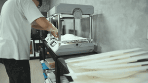 Mass production of off-road tracks in progress, with the operator using the FORMART vacuum forming machine, and pre-printed off-road tracks placed around the area.