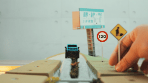 一輛藍色越野車正在模擬賽道上行駛，旁邊有交通標誌和施工標誌，手正放置一個標誌，模擬越野賽道場景